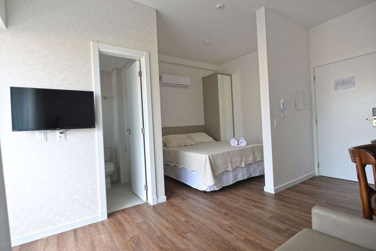 A bedroom with a bed, a TV mounted on the wall, and a door leading to a bathroom.