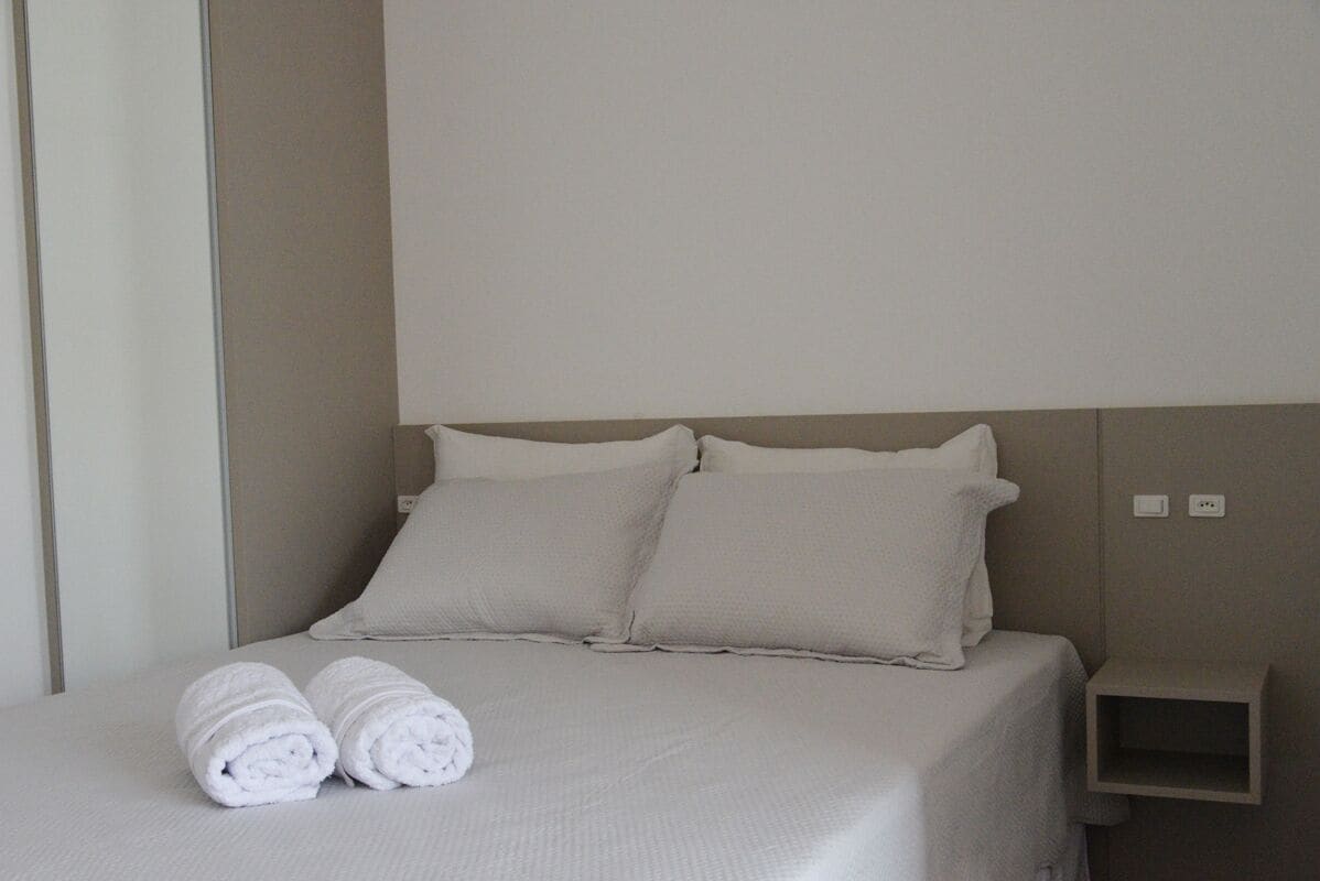 Una cama bien hecha con dos almohadas y dos toallas enrolladas.