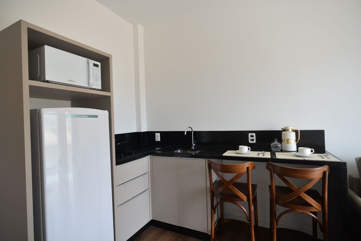 A compact kitchen with a microwave, coffee maker, and two wooden chairs.