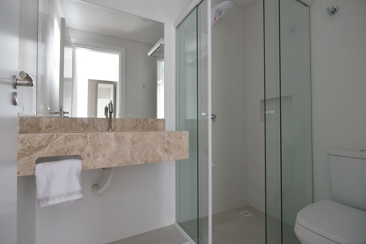 Et moderne badeværelse med et glasbadeafskærmning, en marmorvask og et hvidt toilet.