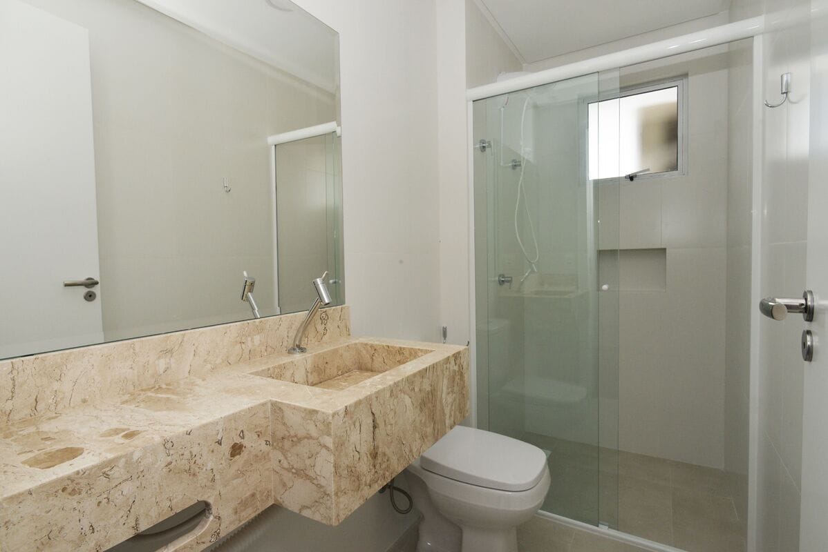 A bathroom with a marble sink, a toilet, and a glass-enclosed shower.