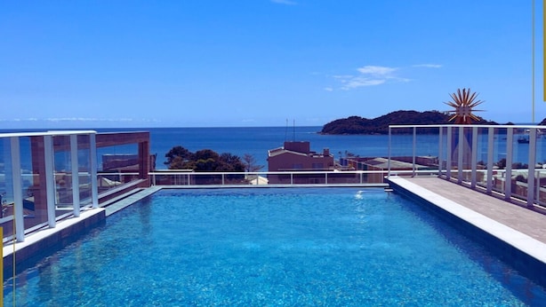 A clear blue swimming pool with a view of the sea and a distant island. - Vila do Centro Apart Hotel (Bombinhas)