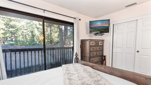 A bedroom with a large sliding glass door leading to a balcony, a wooden dresser, a television on the wall, and a white door. - Snow Summit Getaway - 2-bedroom in Big Bear Lake, Walk to Slopes, Cable TV, Deck, BBQ, Views (Big Bear Lake)