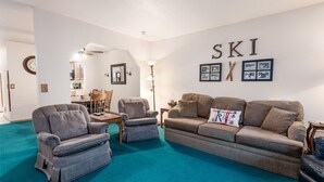 A living room with a blue carpet, two grey armchairs, a brown sofa, and a coffee table. A clock and framed pictures are on the wall. - Snow Summit Getaway - 2-bedroom in Big Bear Lake, Walk to Slopes, Cable TV, Deck, BBQ, Views (Big Bear Lake)