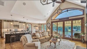 A spacious living room with a large sofa, a coffee table, and a view of a balcony. - Beautiful lakeside family or corporate retreat with pool, hot tub, and  more! (Huddleston)