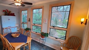 A dining area with a table, chairs, a ceiling fan, a cabinet, and windows with a view of trees. - Beautiful lakeside family or corporate retreat with pool, hot tub, and  more! (Huddleston)