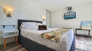 Een keurig opgemaakt bed met een bloemenbedekking, een nachtkastje met een lamp en een schilderij aan de muur.