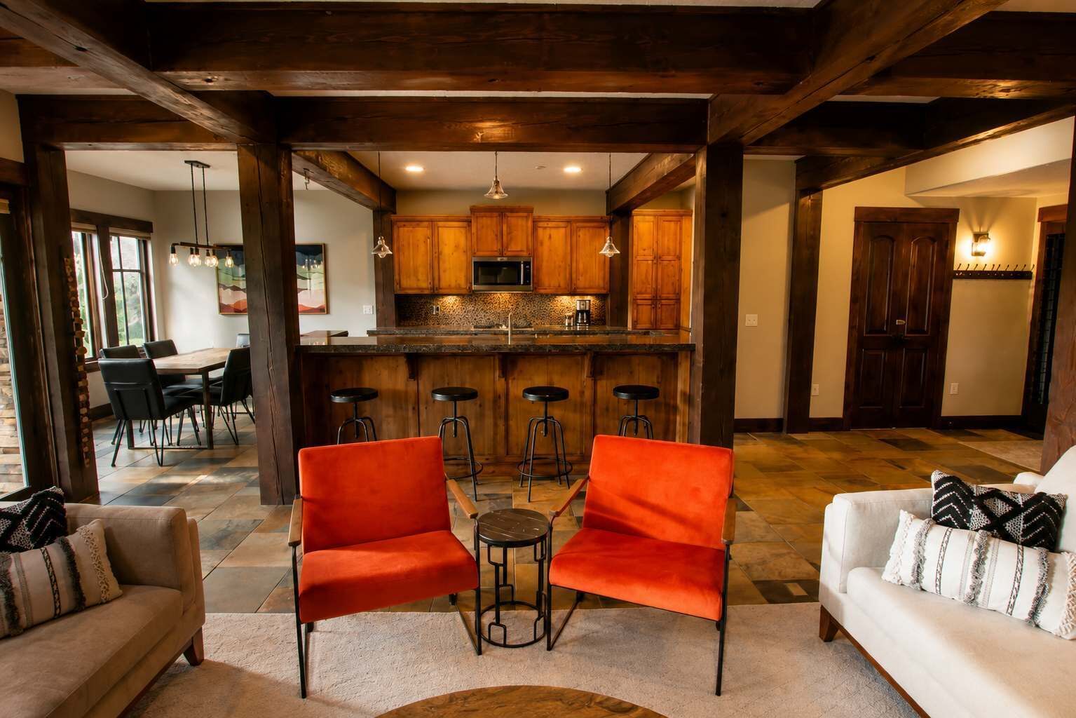 Amplia sala de estar con una cocina al fondo, destacando vigas de madera, una zona de bar y asientos modernos.