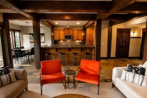 A spacious living area with a kitchen in the background, featuring wooden beams, a bar area, and modern seating. - Powder Mountain Escape • Ski-Inspired (Huntsville)