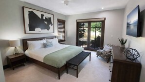 Ein Schlafzimmer mit Bett, Nachttischen, einer Bank, einem Sessel, einem Fernseher und Blick ins Freie.