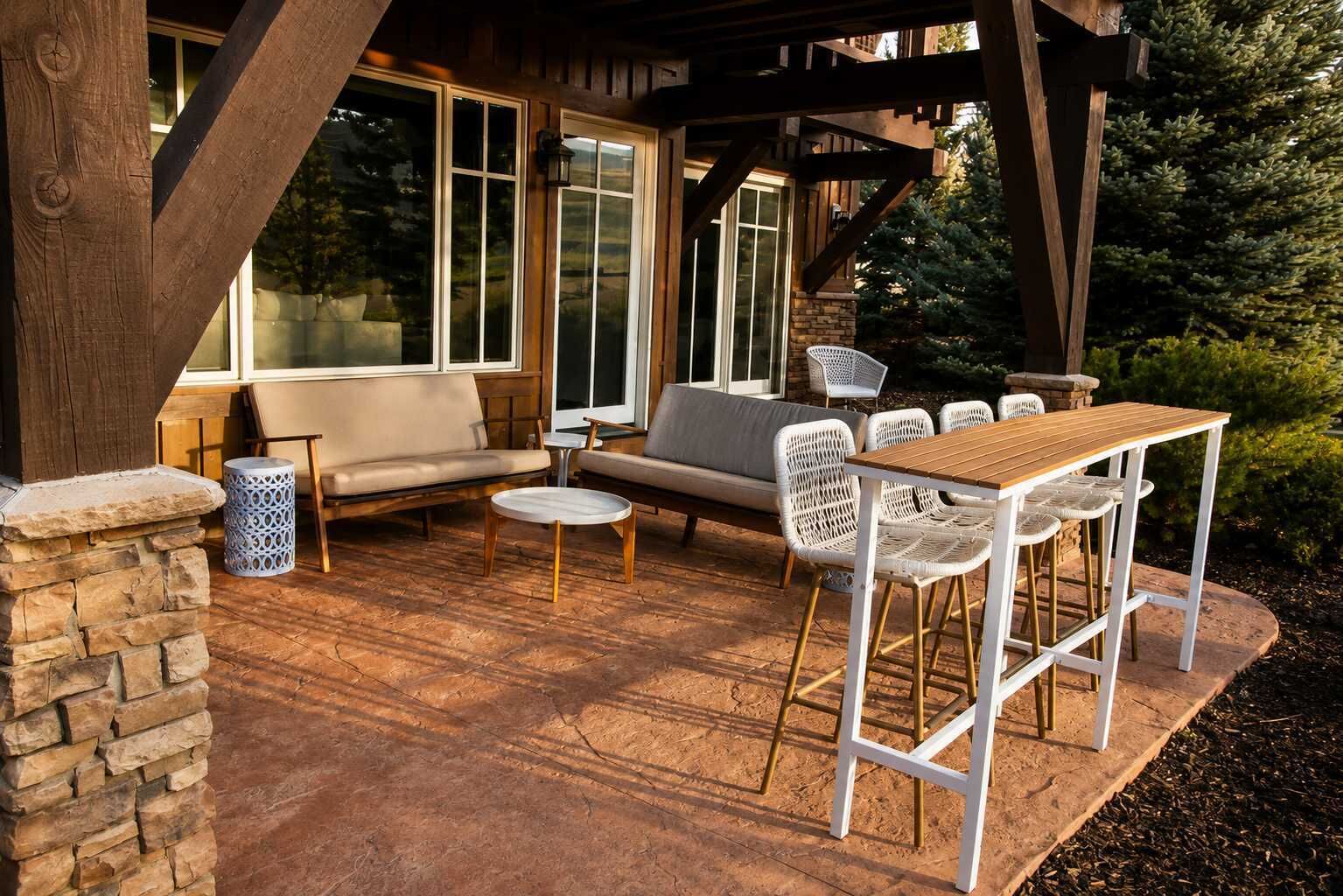 An outdoor patio with a wooden table and chairs, a sofa, and a stone pillar.