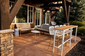 An outdoor patio with a wooden table and chairs, a sofa, and a stone pillar. - Powder Mountain Escape • Ski-Inspired (Huntsville)