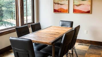 A dining area with a wooden table and black chairs, a hanging light fixture, and two abstract paintings on the wall.