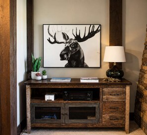 A wooden entertainment center with a mounted picture of a moose, a lamp, and some books.