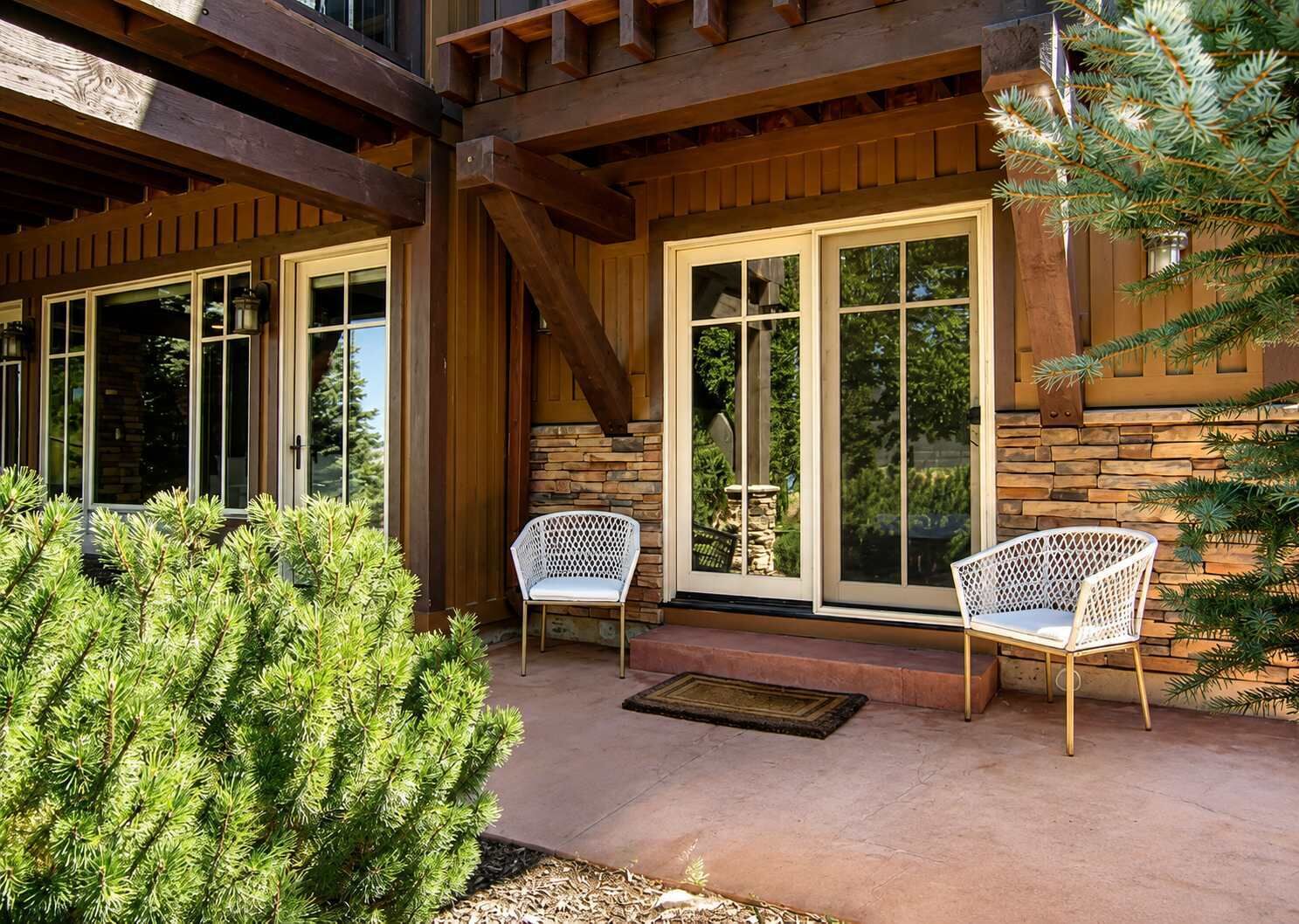 A covered patio with two white chairs and a stone wall.