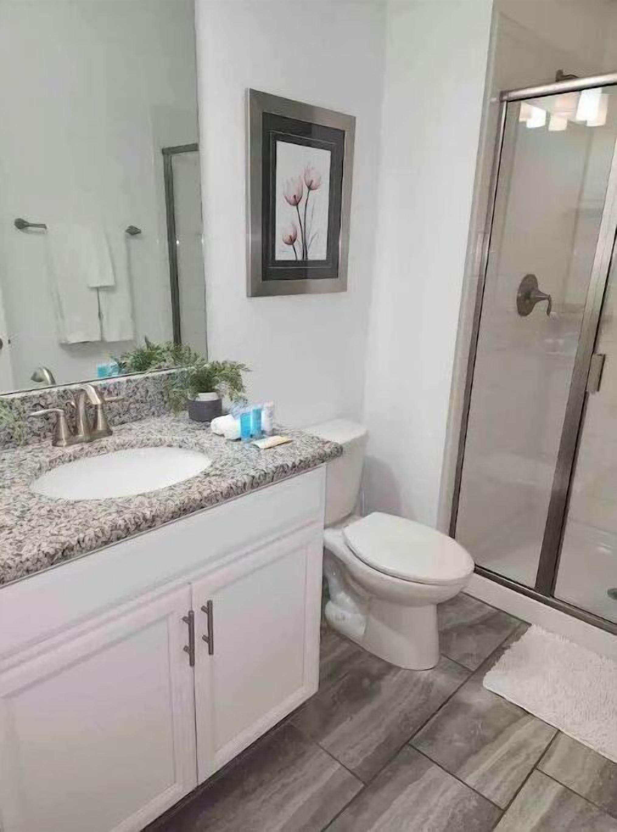 Un baño con lavamanos de encimera de granito, inodoro y cabina de ducha de vidrio.