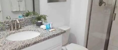 Un baño con lavamanos de encimera de granito, inodoro y cabina de ducha de vidrio.