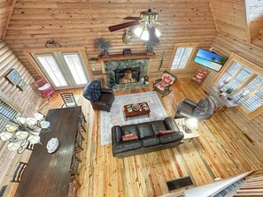A cozy log cabin interior with a fireplace, leather furniture, and a television.