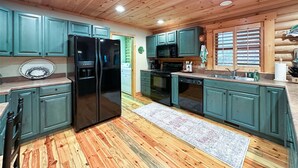 A kitchen with wooden ceiling, teal cabinets, a black refrigerator, and a microwave. - A Log Home Above the Lake | Hickory Hills Cabin (Highlands)