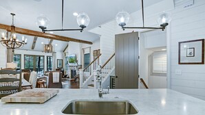 A modern kitchen with a large island, stainless steel sink, and pendant lighting.