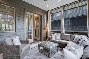 A covered outdoor seating area with a sofa, chairs, and a glass coffee table.