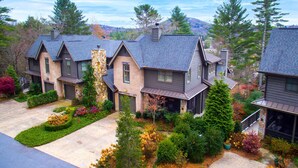 A row of modern houses with stone pillars, surrounded by well-maintained gardens and trees.