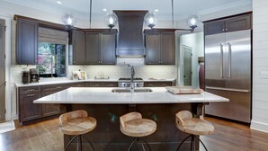 A modern kitchen with dark wood cabinets, a large island with bar stools, stainless steel appliances, and pendant lighting.