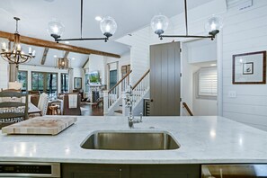 A kitchen with a large island, stainless steel sink, and pendant lighting.