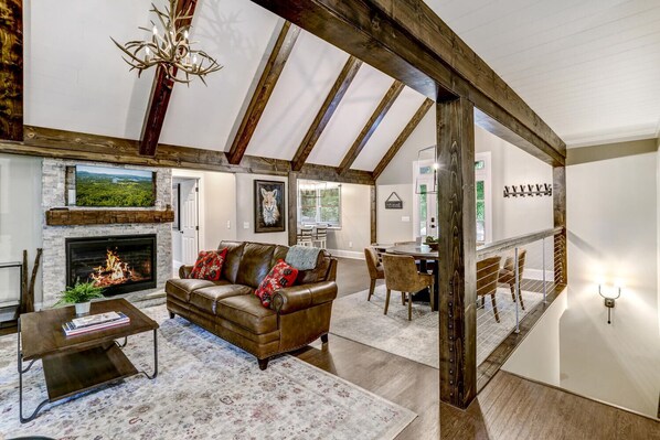 A spacious loft with exposed wooden beams, a fireplace, a leather sofa, and a dining area. - The Lodge That Turned a Vacation Into a Family Tradition | Deer Ridge (Highlands)