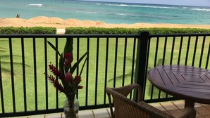 A balcony with a view of the ocean, a small table, and a vase of flowers.
