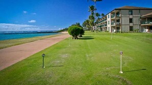 A golf course with a clear view of the ocean, a well-maintained lawn, and a building with multiple balconies.