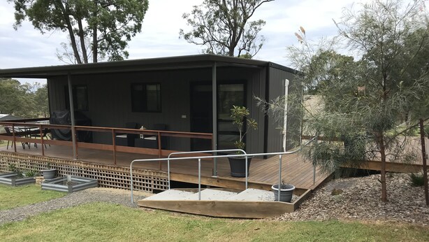 A modern building with a covered outdoor seating area, a wooden deck, and a small garden. - Night retreat in the country (Paterson)