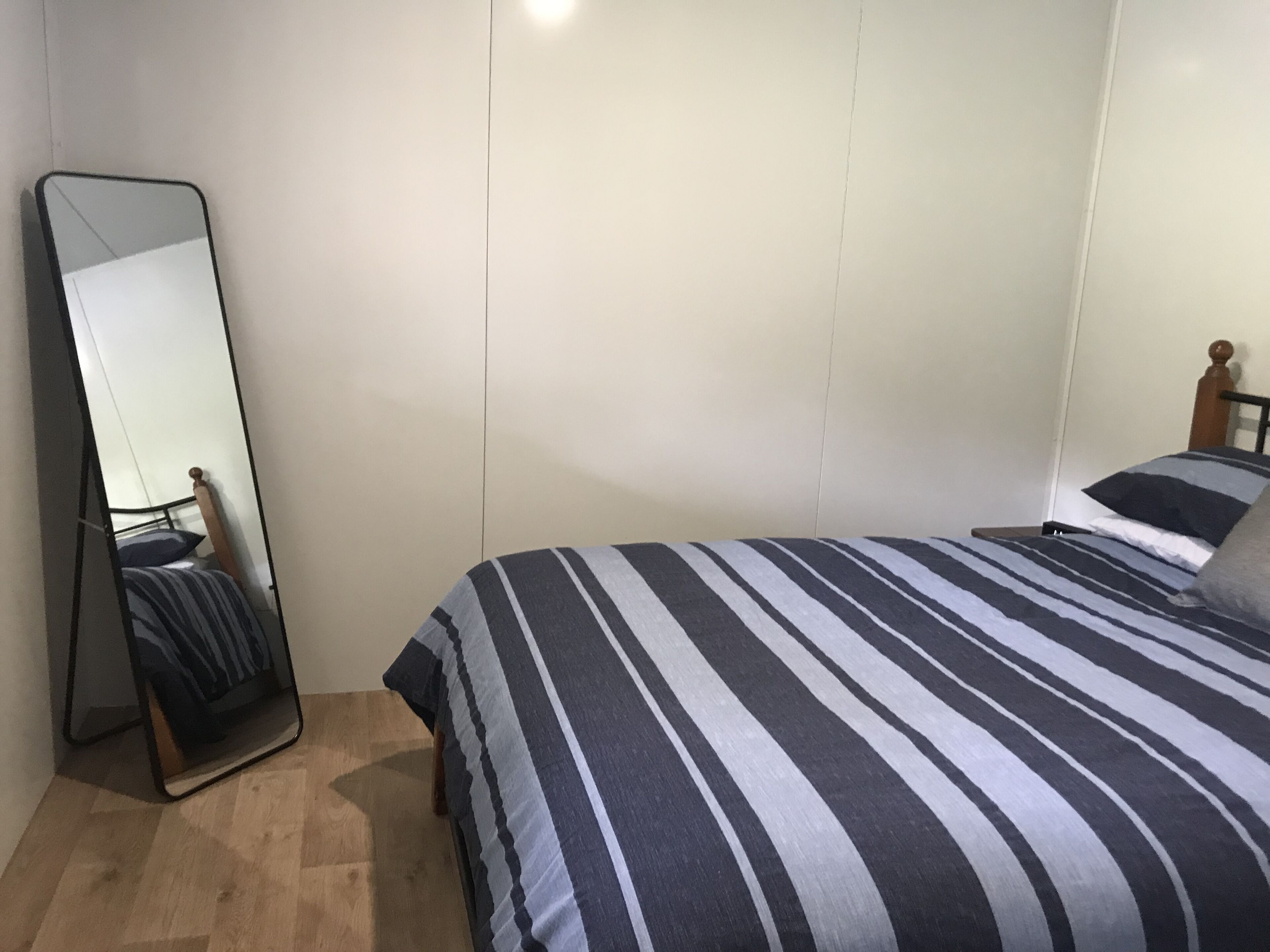 A bedroom with a bed, a large mirror, and a wooden headboard.