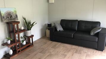 En moderne stue med en sort lædersofa, en træplantestand med potteplanter og et indrammet kunstværk på væggen.