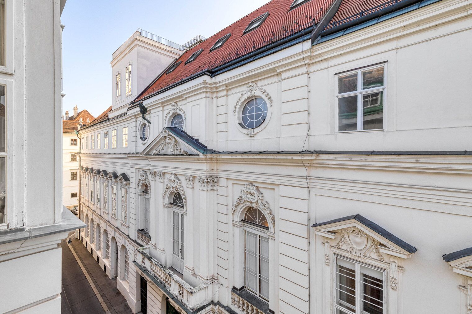 A multi-story building with classical architecture, featuring ornate window frames and a red-tiled roof.
