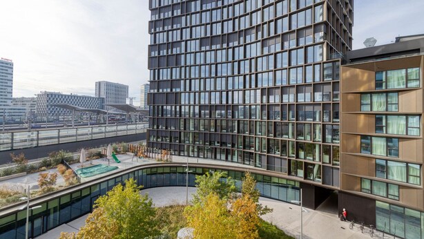 A modern building with a curved glass facade, a rooftop garden with seating, and a view of the cityscape. - Amazing Belview 1BR w/ Gym, Lounge & Elevator, nr Metro, by Blueground (Vienna)