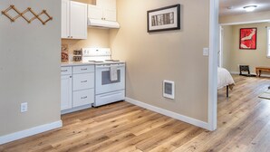 A compact kitchen with white cabinets, a stove, and a vent. A framed picture hangs on the wall, and there's a wooden floor. - Far East Escape: Zen apartment, Japanese tea table (Salem)