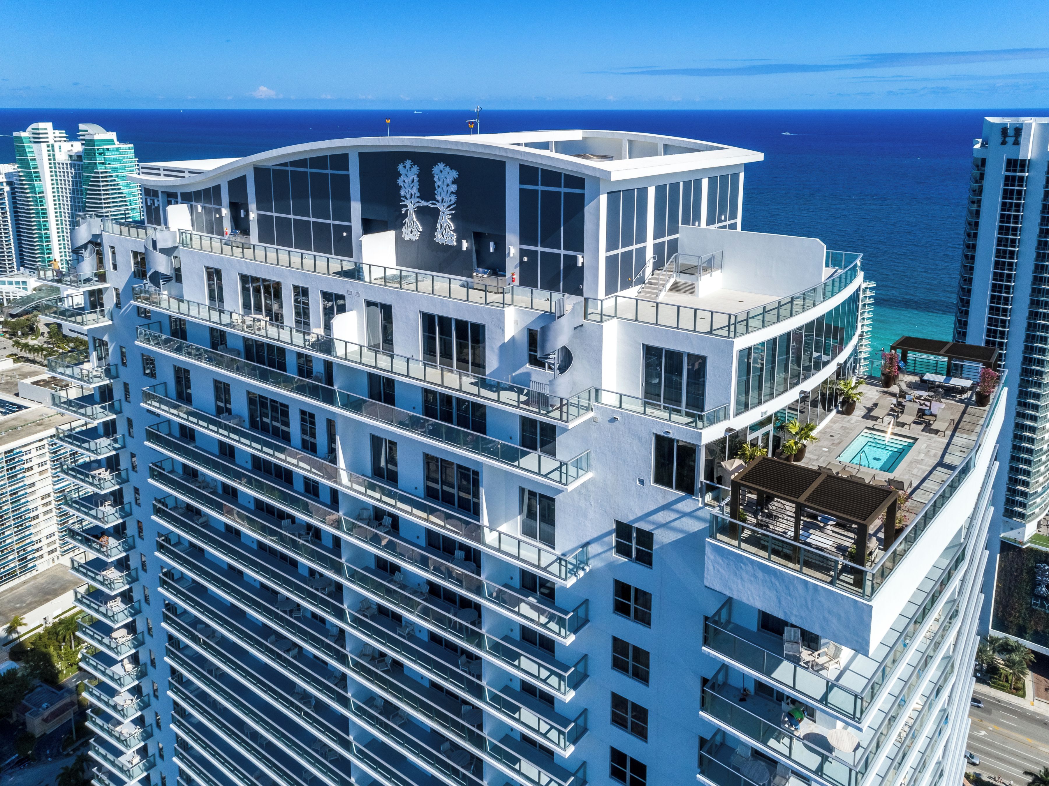 A high-rise hotel with multiple balconies, a rooftop pool, and a view of the ocean.