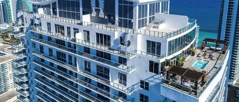 A high-rise hotel with multiple balconies, a rooftop pool, and a view of the ocean.