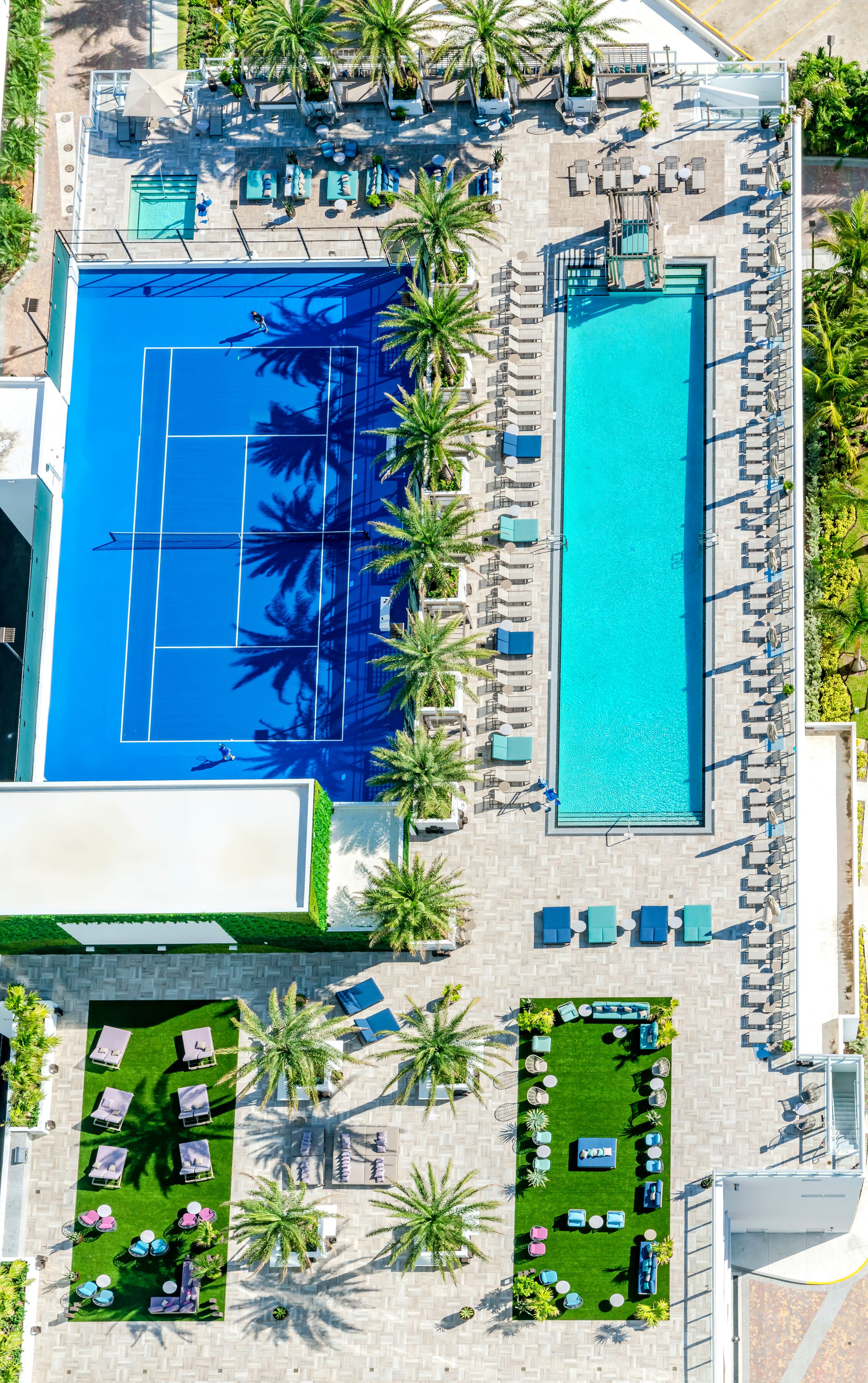 An aerial view of a resort with a large swimming pool, sun loungers, and palm trees.