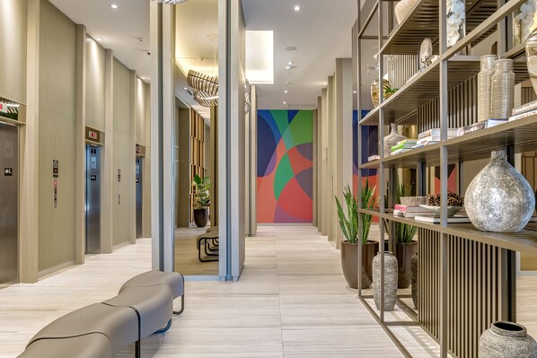 A modern hotel corridor with a seating area, elevators, and a decorative wall with geometric patterns.