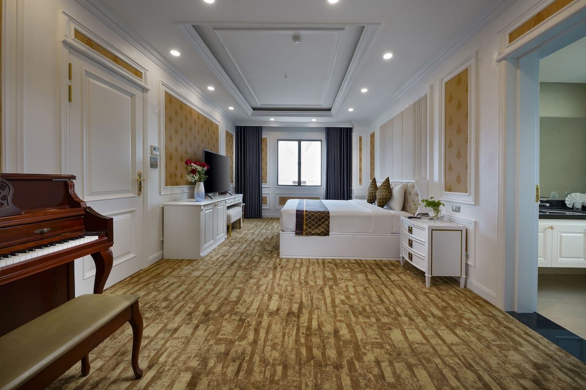 Habitación de hotel con un piano, una cama, un escritorio y un ventanal grande.