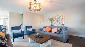 A living room with a grey sofa, two blue armchairs, a wooden coffee table, and a decorative wall piece. - Keuka Sunrise Retreat: "A Lakefront Dream Home" (Branchport)