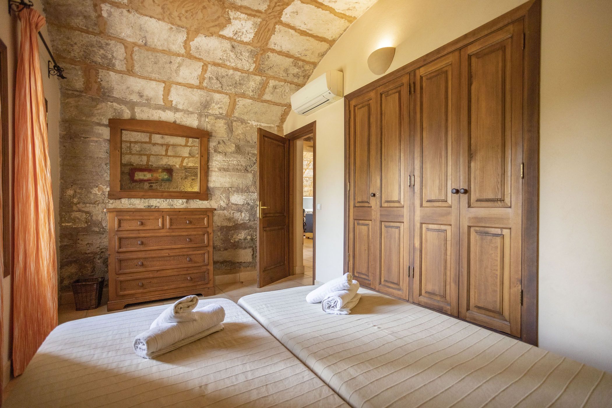 Une chambre avec deux lits, une armoire en bois, un mur en pierre et une petite commode en bois.