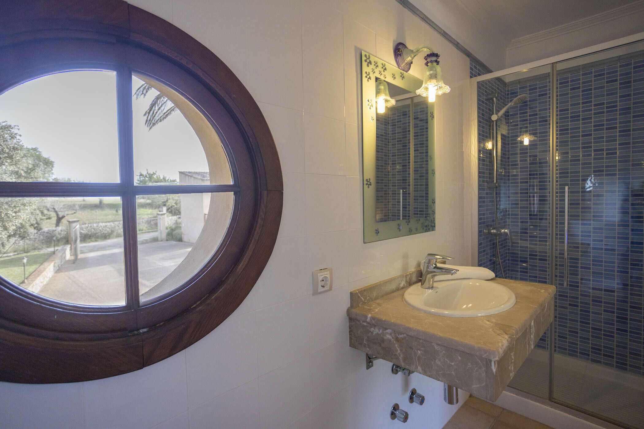 A bathroom with a round window, a sink with a mirror, and a shower area.