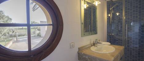 A bathroom with a round window, a sink with a mirror, and a shower area.