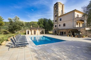 A swimming pool with lounge chairs, a stone building with a tower, and a garden area. - 6 bedroom finca with pool and barbecue (Selva)