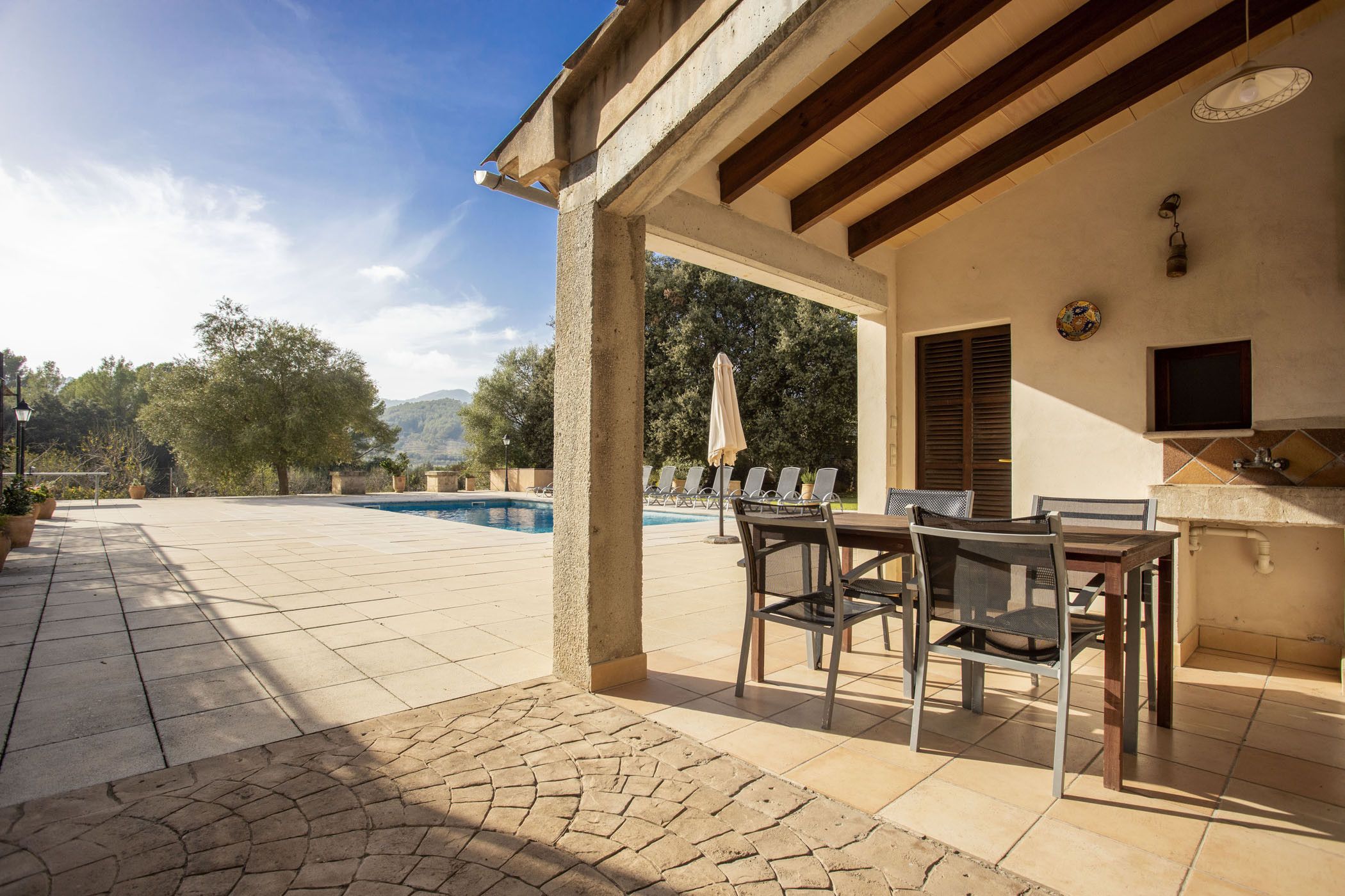Un patio al aire libre con piscina, zona de comedor con sillas y mesa, y espacio de cocina con pileta y mostrador.