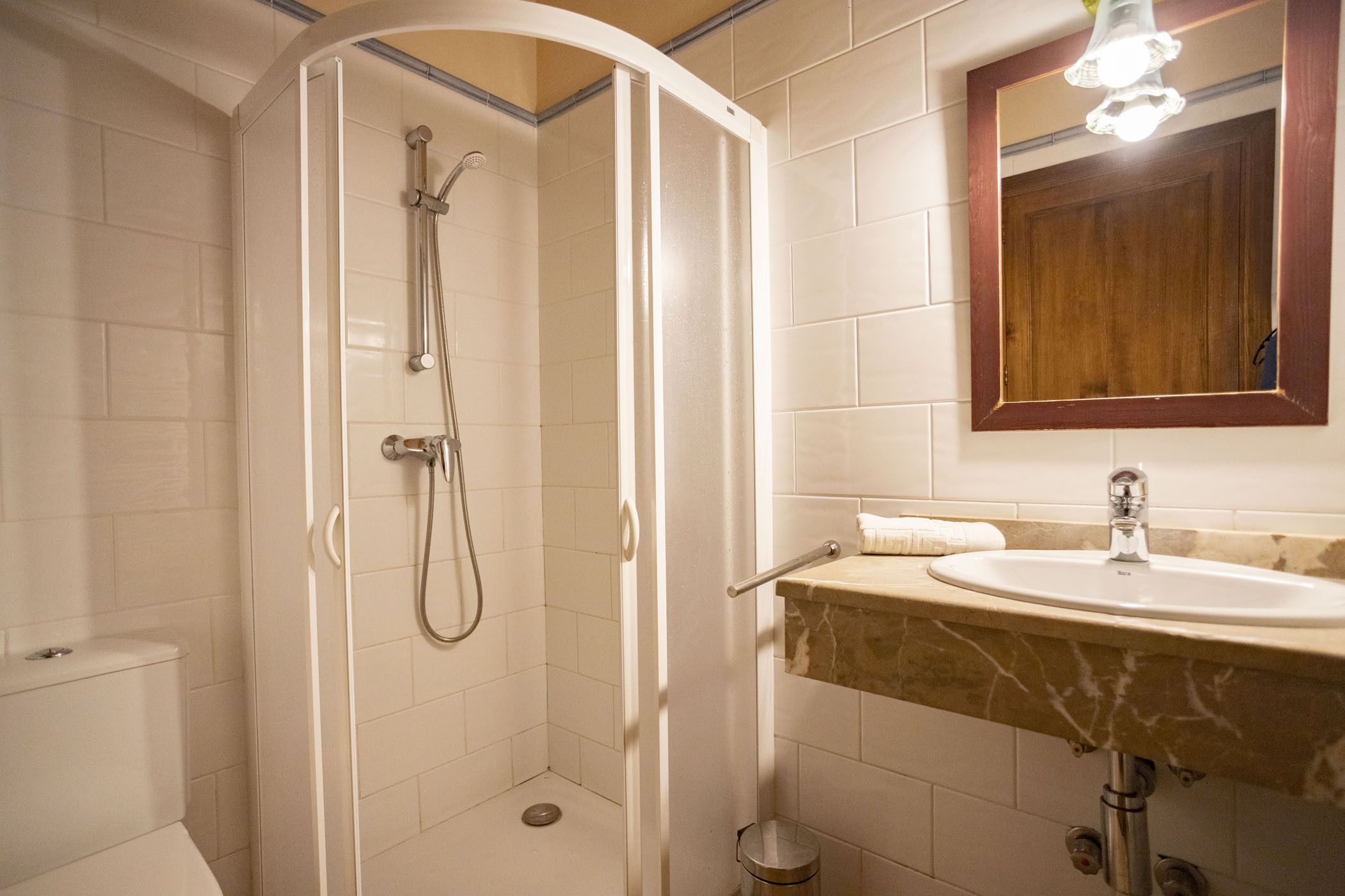A bathroom with a shower, toilet, sink, and mirror.