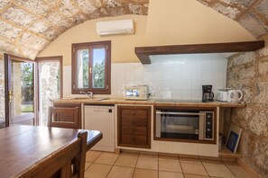 A kitchen with a stone wall, white tiles, wooden cabinets, a dishwasher, a microwave, a coffee maker, and a window with a view of greenery. - 6 bedroom finca with pool and barbecue (Selva)